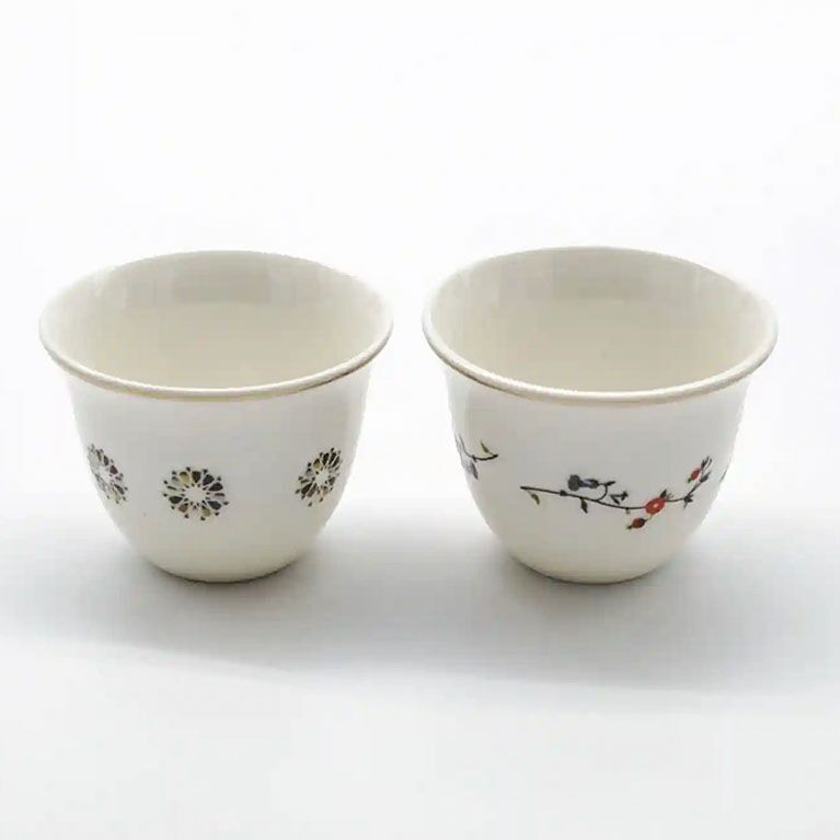 Two porcelain Arabic coffee cups featuring delicate floral and geometric motifs, displayed side by side
